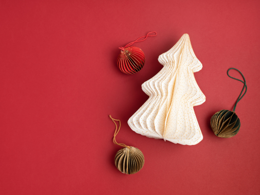 Ein Tannenbaum und Weihnachtskugeln aus Papier auf rotem Untergrund
